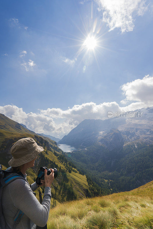 在意大利北部Dolomites的Viel dal Pan小路上，一名年长妇女正在拍摄Fedaia湖和Marmolada湖的美丽景色。